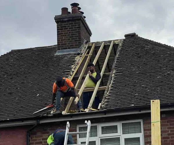 This is a photo of a roof repair being carried out. A section of the roof has been stripped and two roofers are replacing the rafters. Works being carried out by BN Roofing Letchworth Garden City